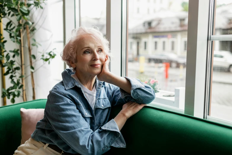 a woman sitting on a green couch next to a window, a portrait, pexels, photorealism, white-haired, thoughtful ), a still of a happy, aged