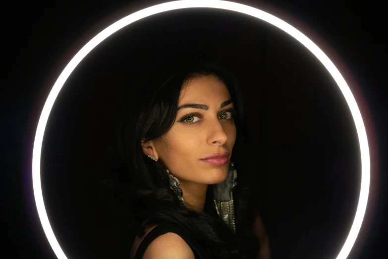 a woman standing in front of a circular light, an album cover, pexels contest winner, hurufiyya, young middle eastern woman, ring light, 8k selfie photograph, black jewellery