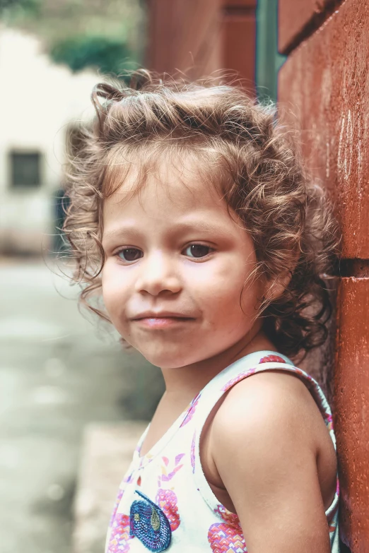 a little girl leaning against a brick wall, pexels contest winner, with textured hair and skin, in sao paulo, fair olive skin, bedhead