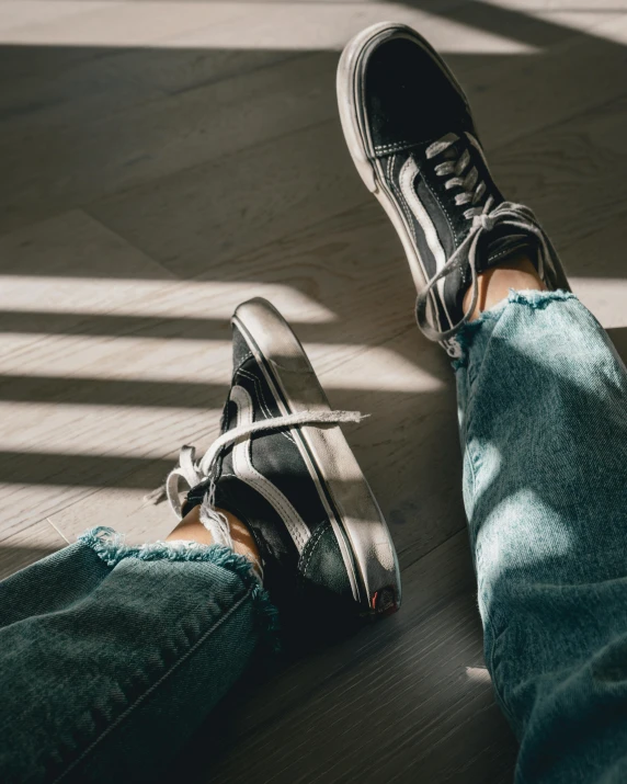 a person sitting on top of a wooden floor, inspired by Elsa Bleda, trending on pexels, hyperrealism, blue jeans and grey sneakers, gradient black to silver, two buddies sitting in a room, sneaker photo