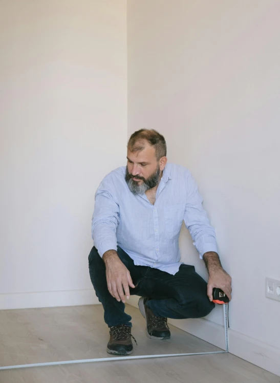 a man kneeling on top of a hard wood floor, by Alexander Fedosav, pexels contest winner, hyperrealism, sitting in an empty white room, grey trimmed beard, gif, construction