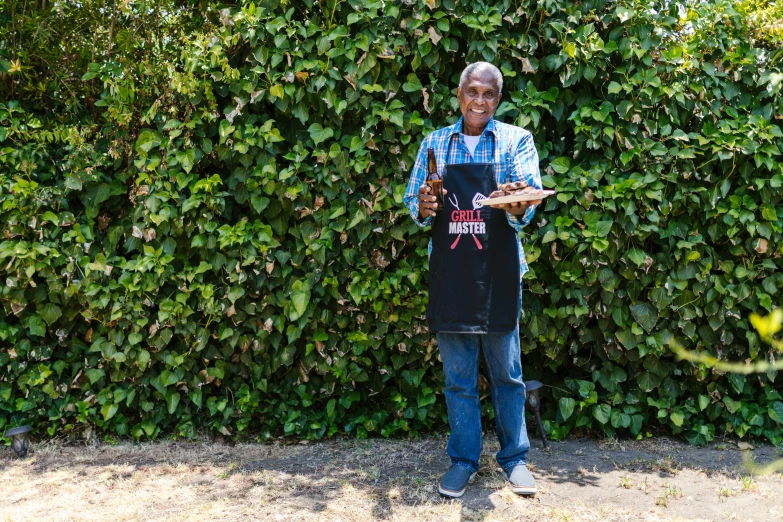 a man that is standing in front of a bush, by Ceferí Olivé, serving rack of ribs, holding a bottle, portrait image, full frame image