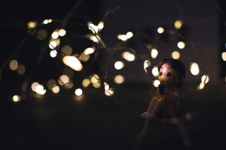 a small figurine sitting in front of a string of lights, inspired by Elsa Bleda, pexels contest winner, magical realism, instagram picture, low - angle shot, toy photo, warm yellow lights