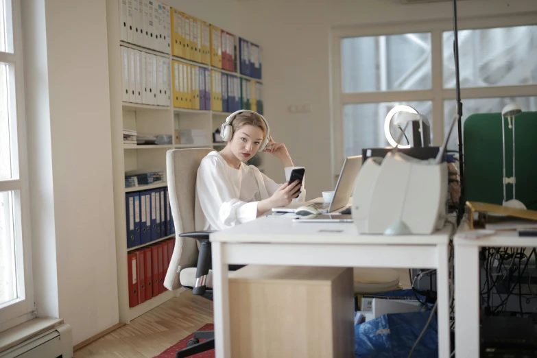 a woman sitting at a desk using a cell phone, pexels, arbeitsrat für kunst, headphones on head, low quality photo, a blond, a wide shot