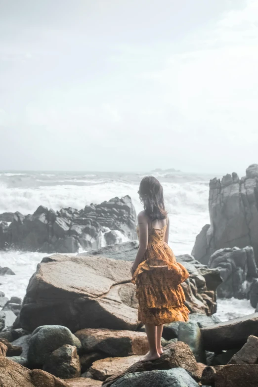 a woman standing on a rocky beach next to the ocean, pexels contest winner, romanticism, sri lanka, long hair windy, taiwan, instagram photo