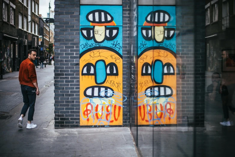 a man standing in front of a wall with graffiti on it, by Doug Ohlson, pexels contest winner, street art, elevator doors look like a mouth, two heads, orange and cyan paint decals, in london