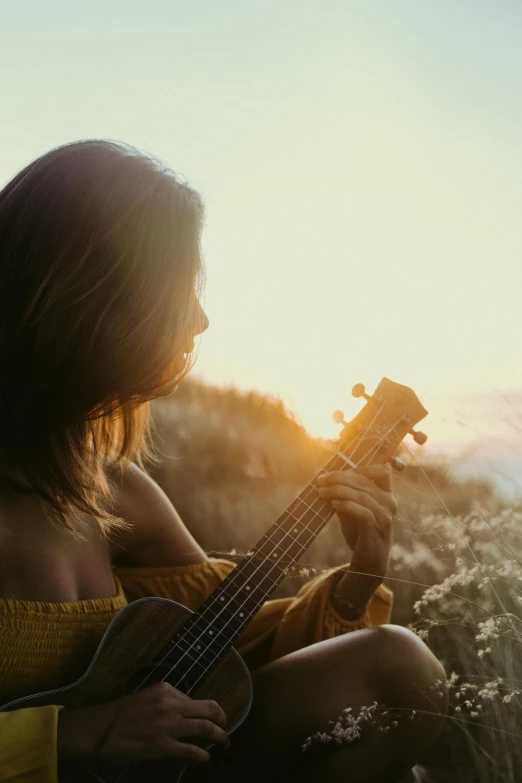 a woman sitting in a field playing a guitar, pexels contest winner, romanticism, looking off into the sunset, ukulele, paul barson, bright sunny time