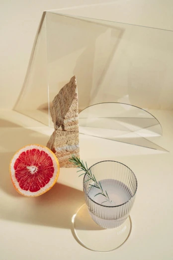 a grapefruit and a glass of water on a table, a still life, by Nathalie Rattner, featured on pinterest, folded geometry, transparent corrugated glass, dynamic angled shot, large tall