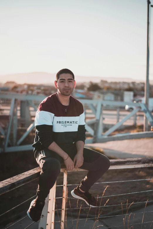 a man sitting on a rail in a parking lot, by Robbie Trevino, standing on a bridge, wearing casual clothes, ramil sunga, profile image