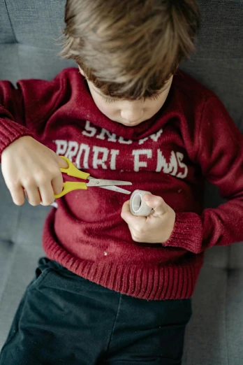 a young boy holding a pair of scissors, pexels contest winner, red sweater and gray pants, hot glue, maroon, miniature faking