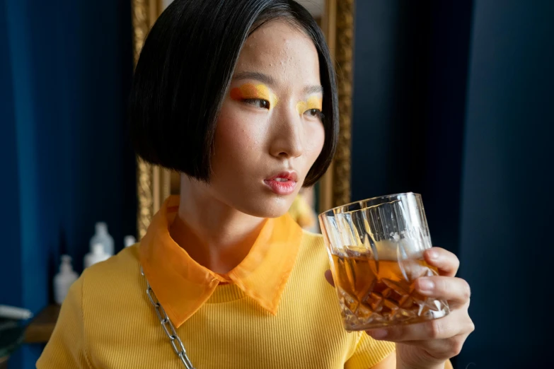 a woman holding a glass of whiskey in front of her face, inspired by Georges de La Tour, trending on unsplash, hyperrealism, kiko mizuhara, yellow makeup, traditional chinese clothing, square rimmed glasses