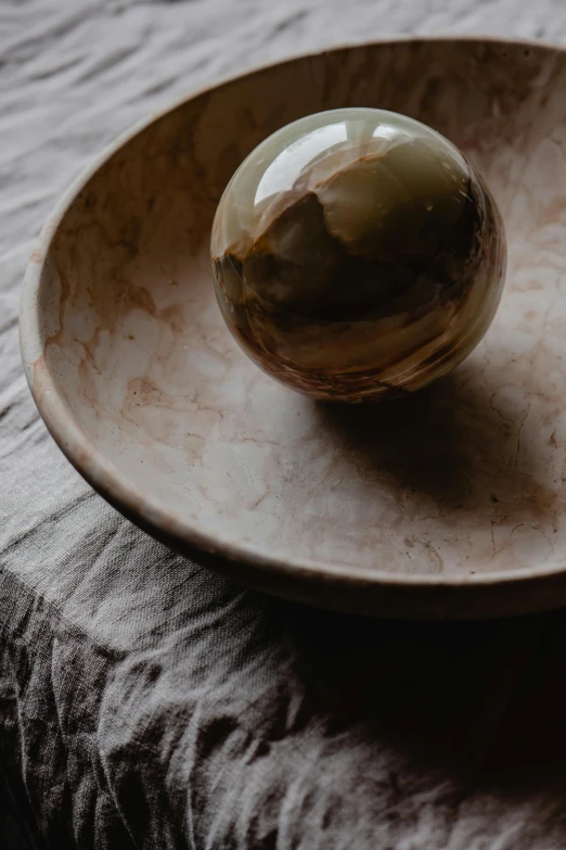 a marble ball sitting on top of a wooden plate, by Rebecca Horn, trending on unsplash, visual art, ochre, taupe, made of silk paper, bowl