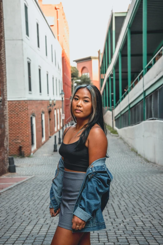 a woman standing in the middle of a brick road, an album cover, inspired by helen huang, trending on unsplash, realism, wearing a cropped black tank top, standing in a city center, in savannah, cropped shirt with jacket