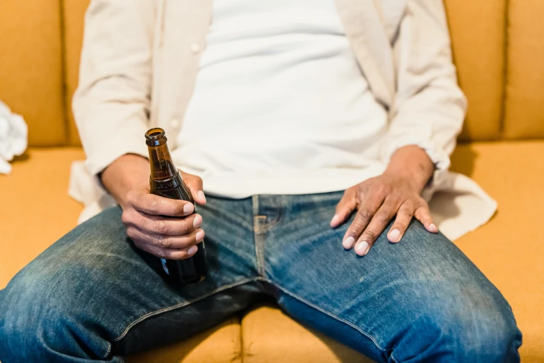 a man sitting on a couch holding a bottle of beer, by Carey Morris, pexels, renaissance, wearing jeans, straya, cysts, waiting to strike