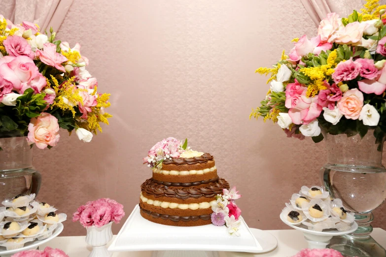 a cake sitting on top of a table next to vases of flowers, brown and pink color scheme, unedited, snacks, mid - shot