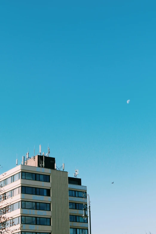 a couple of tall buildings sitting next to each other, a photo, unsplash, postminimalism, crescent moon, sky blue, analog photo, flying in the sky