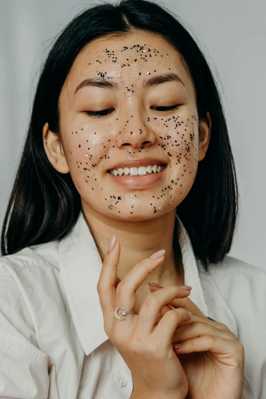 a woman with black spots on her face, trending on pexels, joy ang, black tar particles, textured base ; product photos, grey