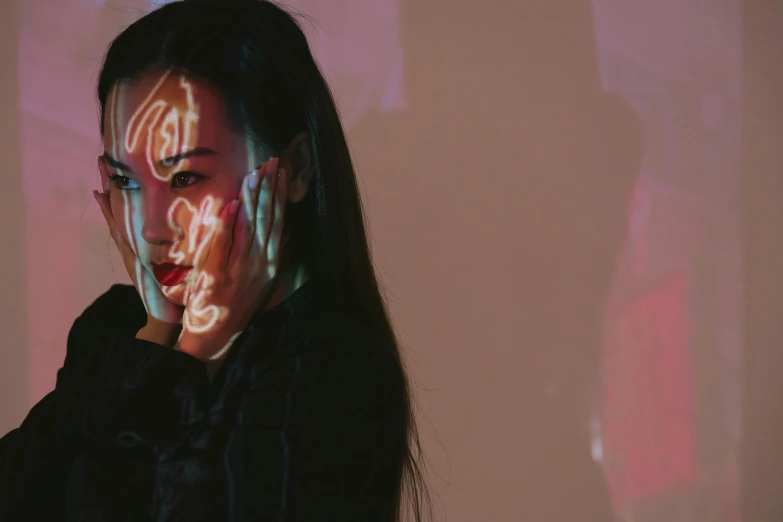 a woman with neon paint on her face, a hologram, pexels contest winner, hyperrealism, a young asian woman, hands shielding face, subtle and compelling lighting, distorted photo