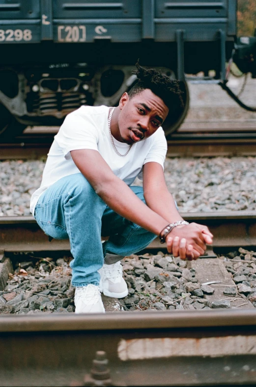 a man sitting on a train track next to a train, an album cover, by Everett Warner, trending on pexels, playboi carti portrait, confident stance, looking left, promotional image