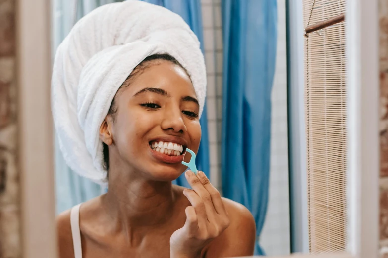 a woman brushing her teeth in front of a mirror, pexels contest winner, happening, underbite, wearing a towel, manuka, white teeth