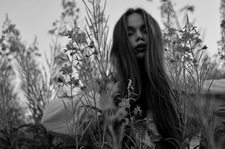 a woman with long hair standing in a field of flowers, a black and white photo, by Emma Andijewska, soft devil queen madison beer, overgrown with orchids, roots and hay coat, close-up portrait film still