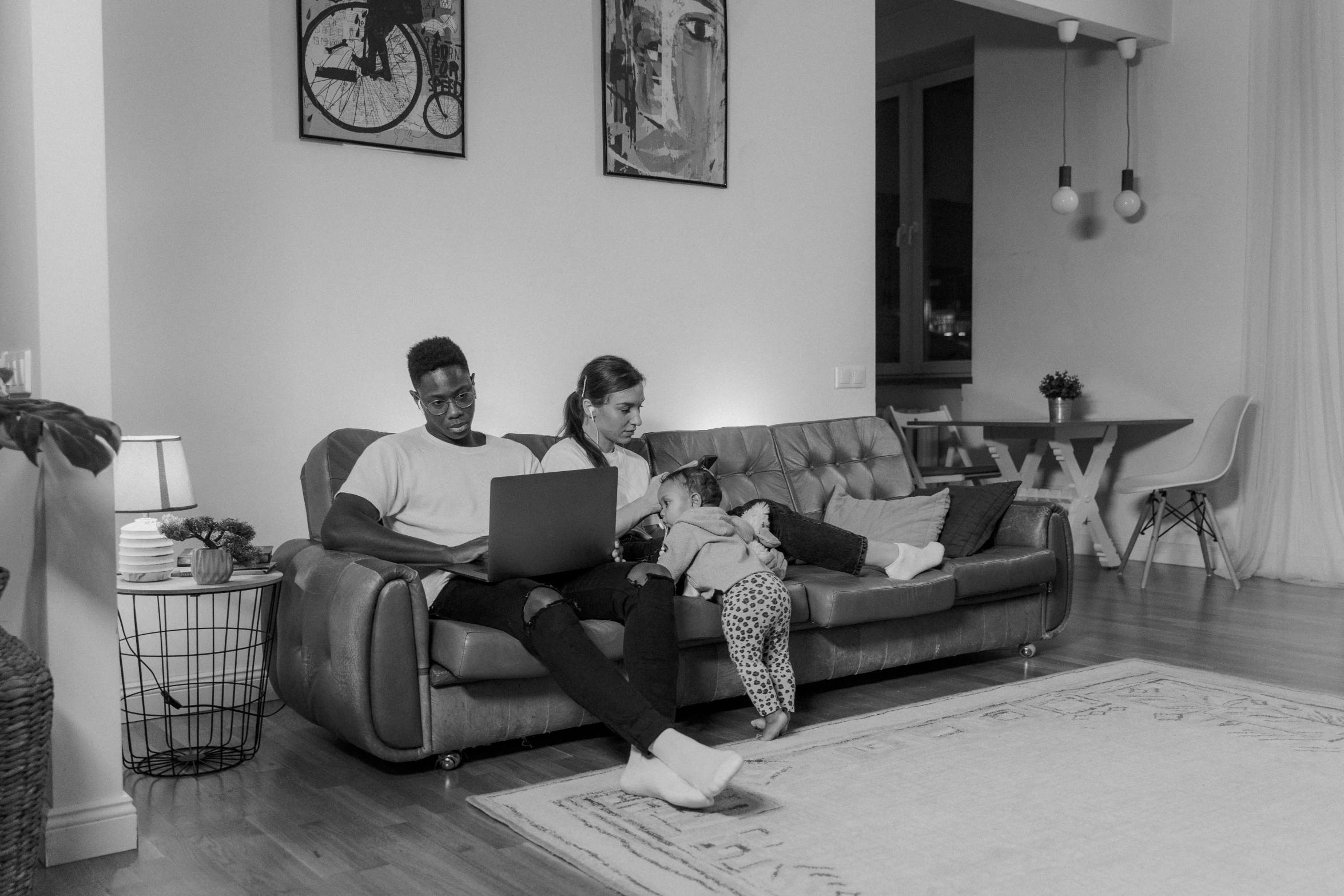 a man and woman sitting on a couch in a living room, a black and white photo, by Adam Marczyński, pexels, programming, portrait of family of three, black people, computer