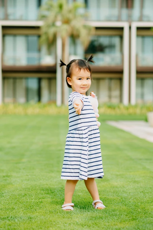 a little girl standing on top of a lush green field, inspired by Cui Bai, unsplash, wearing stripe shirt, confident stance, in a dress, navy