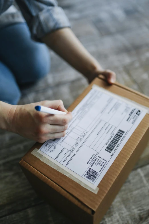 a woman sitting on the floor writing on a piece of paper, by Eden Box, pexels contest winner, mail art, delivering packages for amazon, medium closeup, ship, label