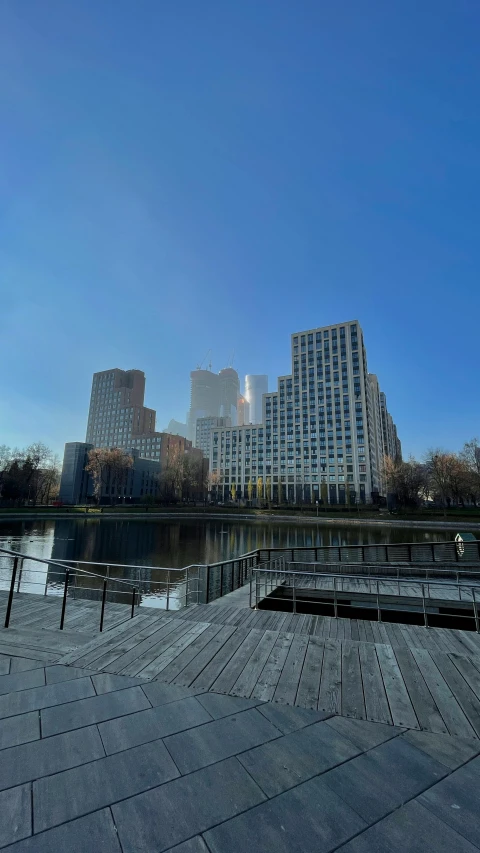 a man riding a skateboard down a sidewalk next to a body of water, mist below buildings, berlin park, frank gehry, 2022 photograph