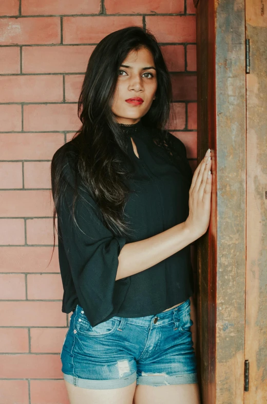 a woman standing in front of a brick wall, black shirt, indian super model, round-cropped, ad image