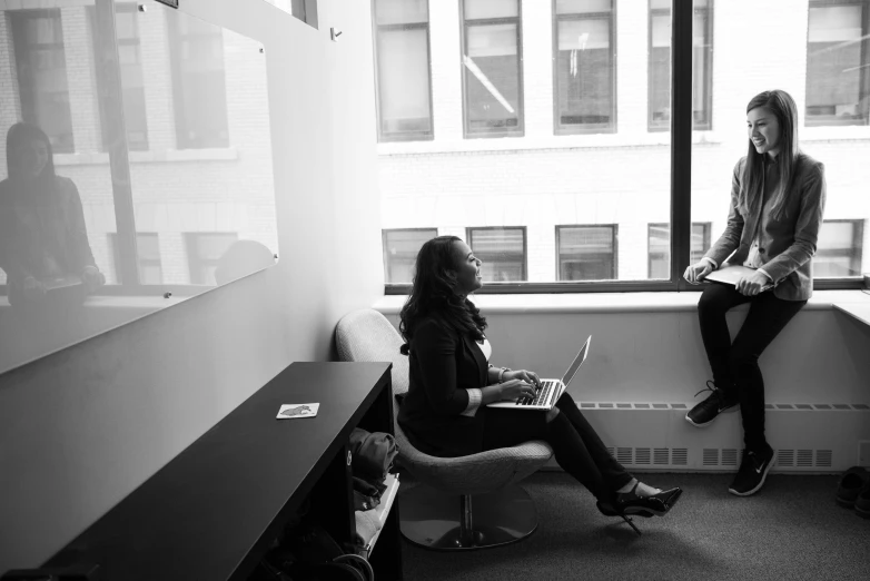 a couple of women sitting on top of a window sill, a black and white photo, by David Palumbo, pexels, in a open-space working space, sitting in dean's office, black female, by greg rutkowski