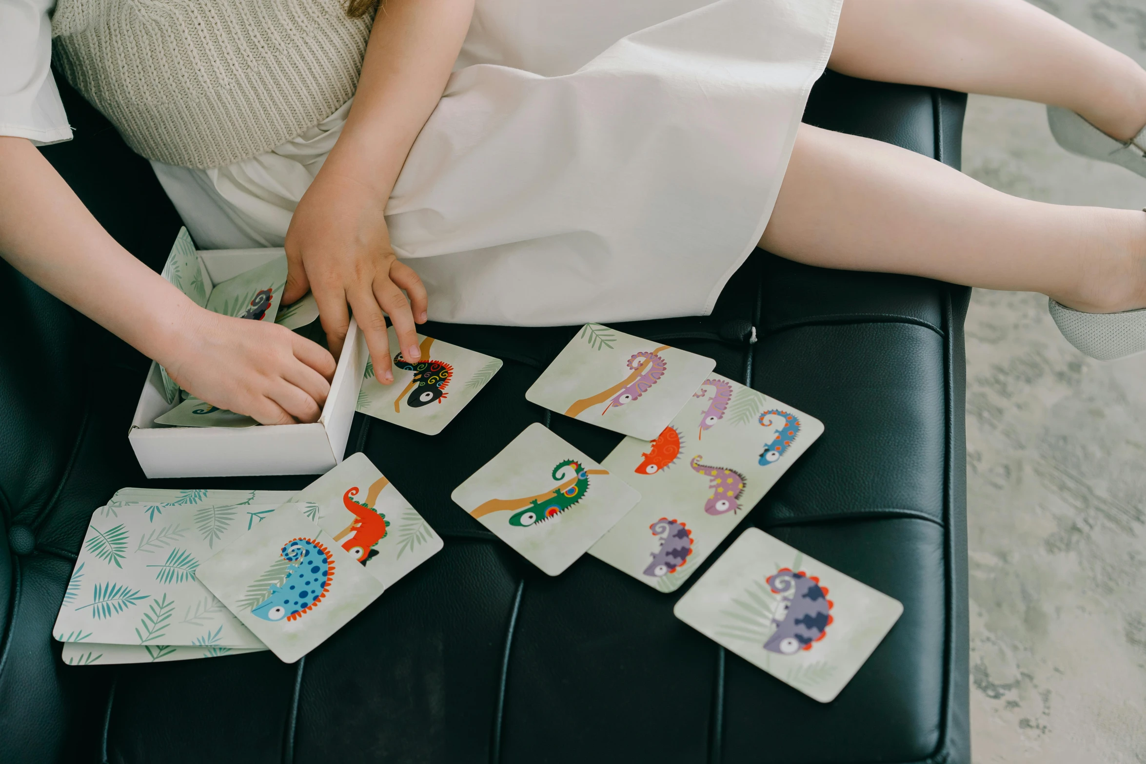 a woman in a white dress sitting on a black bench, a jigsaw puzzle, by Emma Andijewska, trending on pexels, pokemon cards, sitting on a sofa, kids playing, plush leather pads