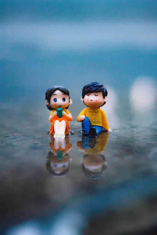 a couple of figurines sitting on top of a table, a picture, unsplash, wet puddles reflecting, cute boys, matching colors, multiple stories