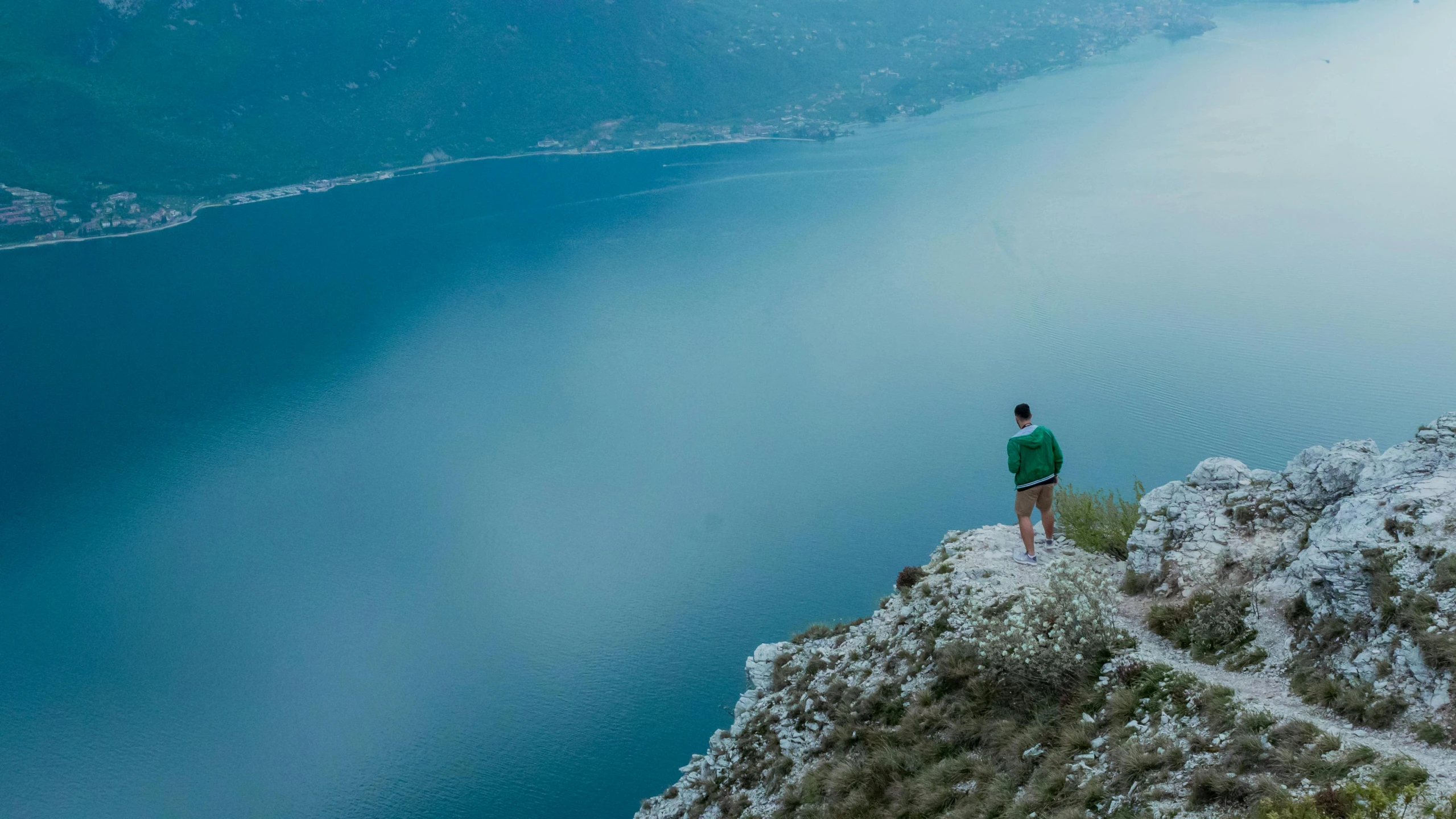 a man standing on top of a mountain next to a body of water, by Niko Henrichon, pexels contest winner, blue and green water, al fresco, slide show, 5 feet away