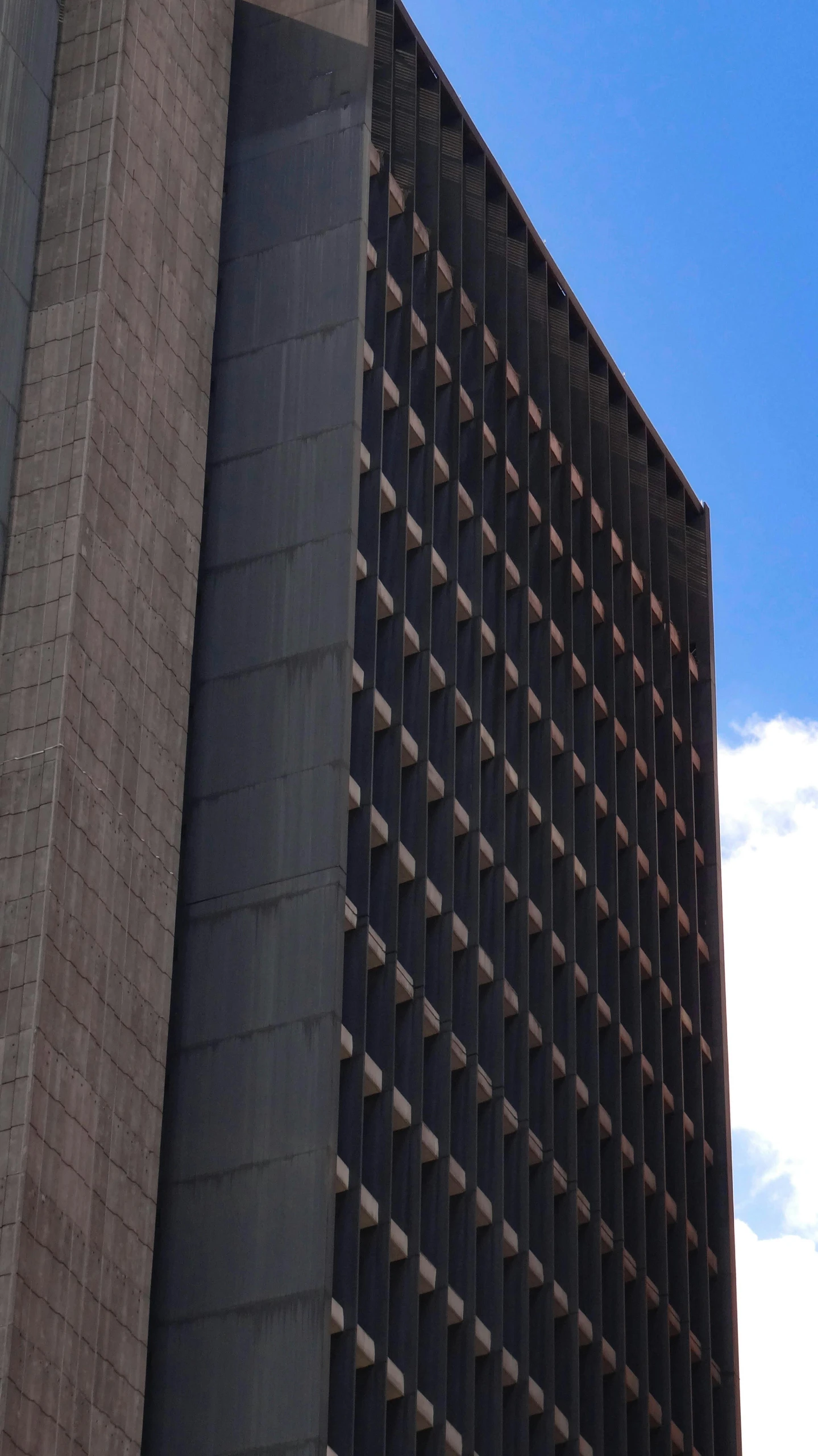 a clock that is on the side of a building, by Pablo Rey, brutalism, towering high up over your view, capital plaza, 1960s color photograph, panoramic shot