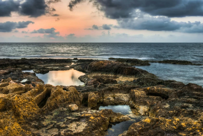 a large body of water sitting on top of a rocky beach, by Daniel Seghers, pexels contest winner, israel, cloudy sunset, coral reefs, iron smelting pits