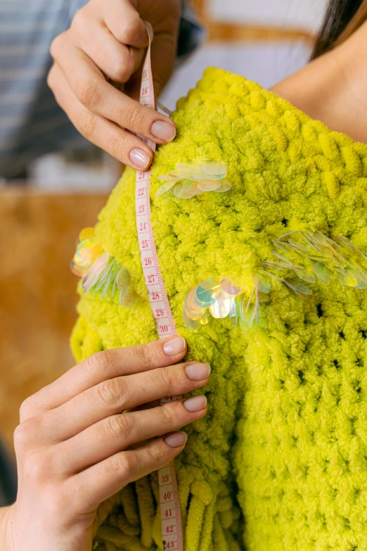 a woman in a yellow sweater holding a measuring tape, inspired by Bernat Sanjuan, iridescent details, fuzzy details, fluo details, embellishment