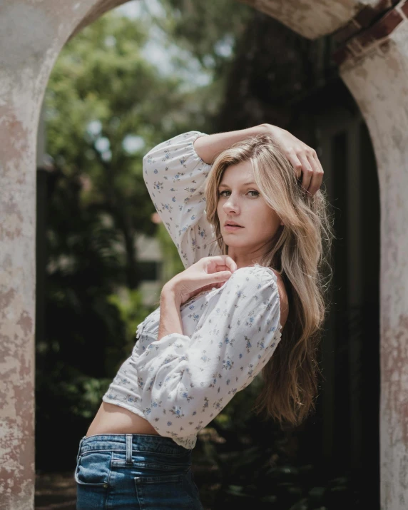 a woman standing in a doorway with her hands on her head, inspired by Beatrice Huntington, trending on unsplash, renaissance, wearing a sexy cropped top, wearing a shirt and a jean, with long blond hair, outdoor photo