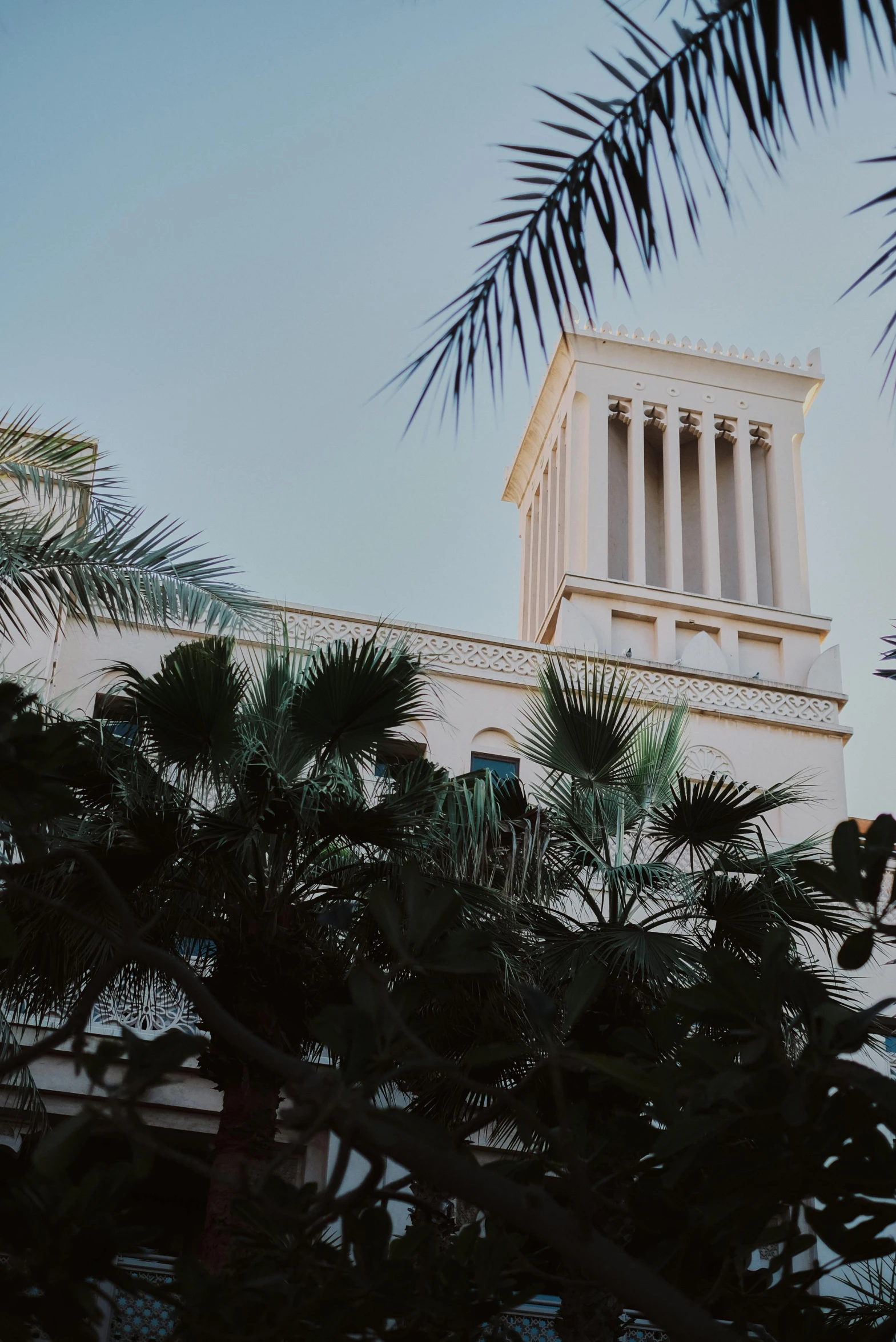 a clock that is on the side of a building, a polaroid photo, unsplash, neoclassicism, with palm trees and columns, arabia, towering high up over your view, roof with vegetation