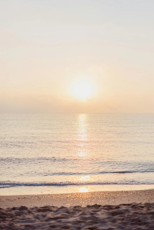 a man riding a surfboard on top of a sandy beach, trending on unsplash, minimalism, at sunrise in springtime, an expansive view of the sun, calm sea, halogen