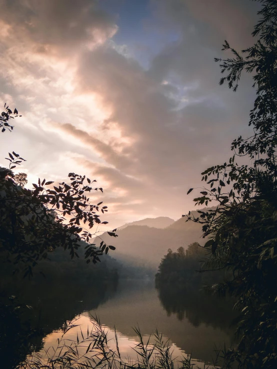 a body of water surrounded by trees under a cloudy sky, pexels contest winner, sumatraism, sunset in a valley, assamese aesthetic, soft light misty, today\'s featured photograph 4k