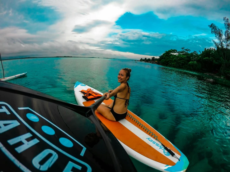 a woman riding a surfboard on top of a body of water, with a roof rack, orange and blue tones, gopro, crystal clear neon water