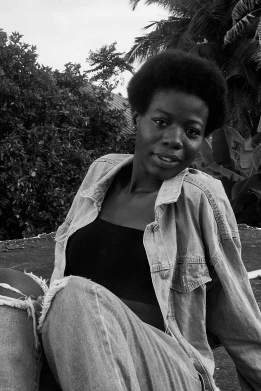 a black and white photo of a woman sitting on a wall, an album cover, by Clifford Ellis, afro hair, grassy knoll, in africa, slightly smiling