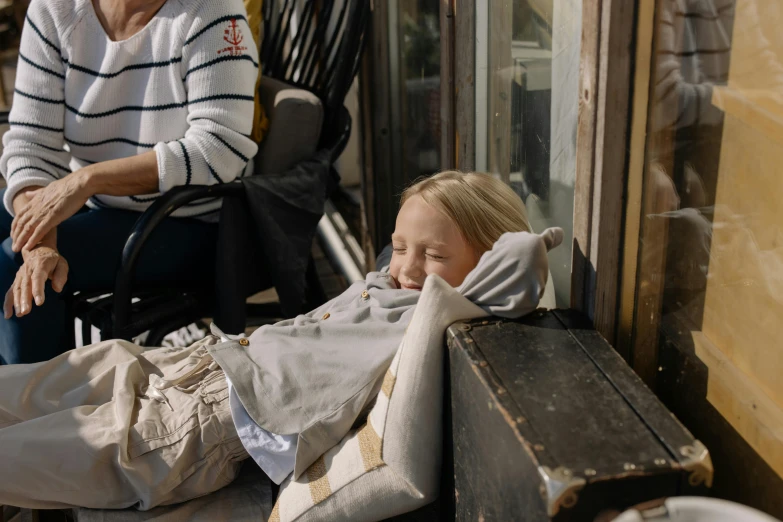 a woman sitting on a bench next to a little girl, sleeping bag, weta workshop, portrait featured on unsplash, people watching around