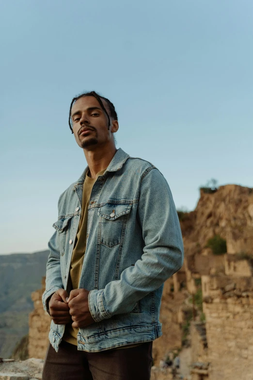 a man standing on top of a mountain next to a cliff, an album cover, pexels contest winner, renaissance, wearing a jeans jackets, middle eastern, joe taslim, profile image