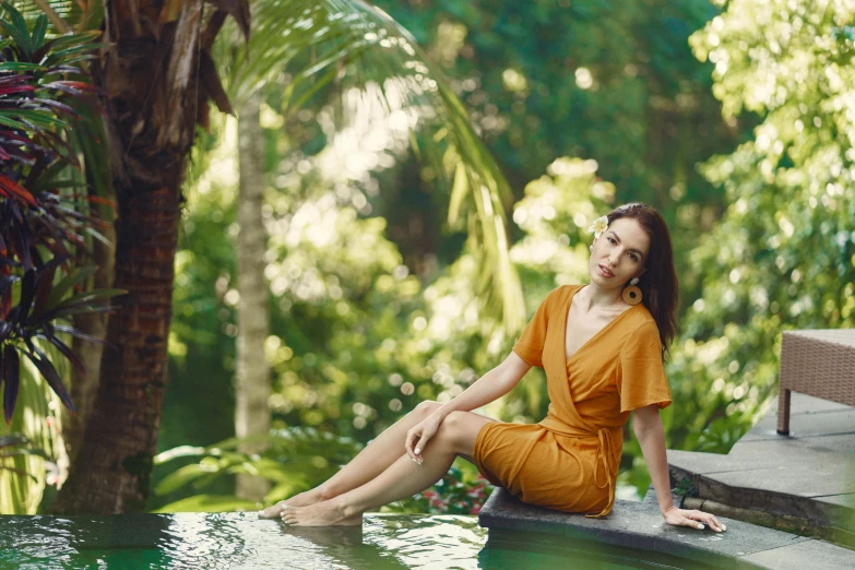 a woman sitting on the edge of a swimming pool, a portrait, by Julia Pishtar, sumatraism, orange jumpsuit, avatar image, lush surroundings, thumbnail