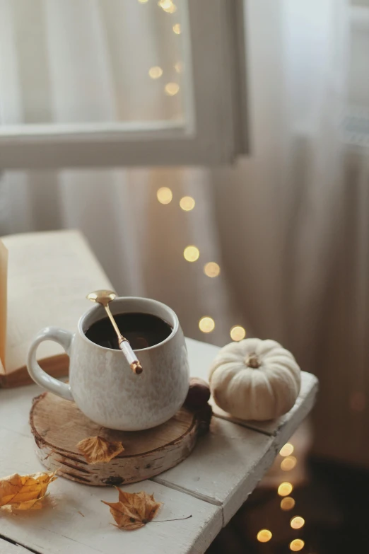 a cup of coffee sitting on top of a wooden table, a still life, by Elaine Hamilton, trending on pexels, magical realism, soft diffuse autumn lights, wooden magic wand, white and gold color palette, pumpkin