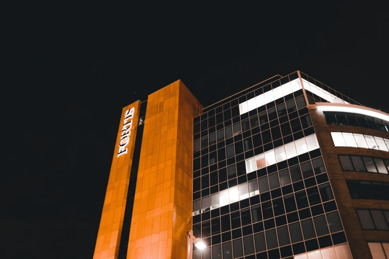 a tall building is lit up at night, a photo, pexels contest winner, brutalism, black and orange, staples, thumbnail, bright signage