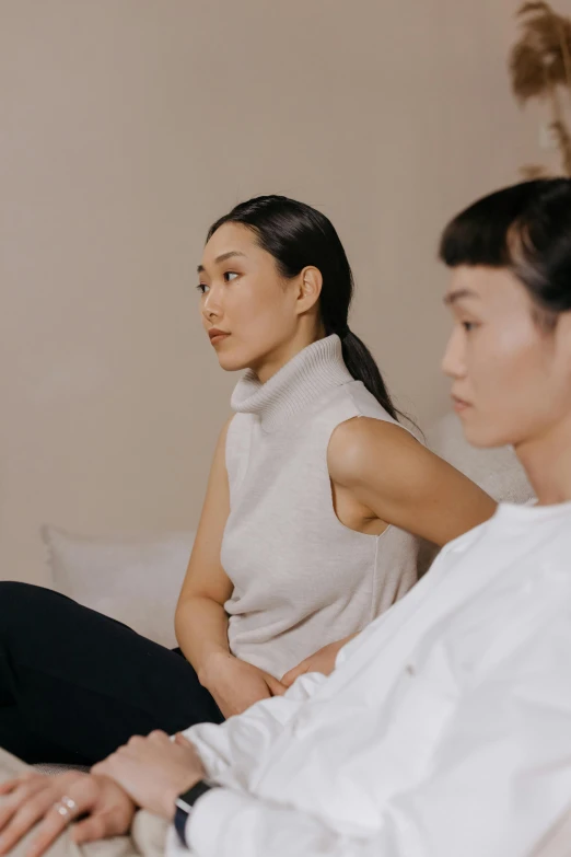 a man and a woman sitting on a bed, inspired by Wang Duo, trending on pexels, visual art, sleeveless turtleneck, asian women, audience, facing sideways