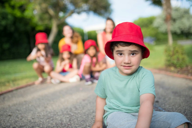 a young boy in a red hat sitting on a skateboard, by Lilia Alvarado, pexels contest winner, group photo, red birthmark, picnic, avatar image